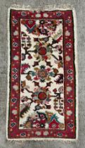 A Caucasian rug having a repeating floral motifs on a cream ground within a red and floral border,