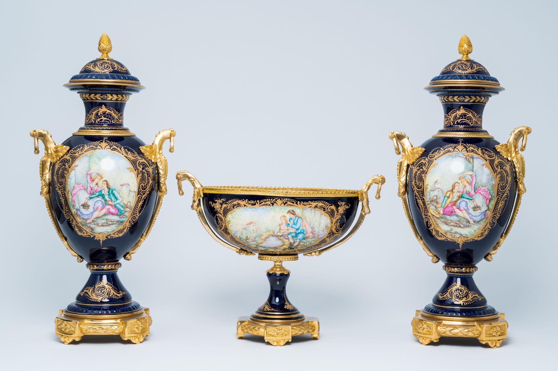 A French gilt mounted blue ground gold layered three-piece garniture with lovely scenes by Lebret, S