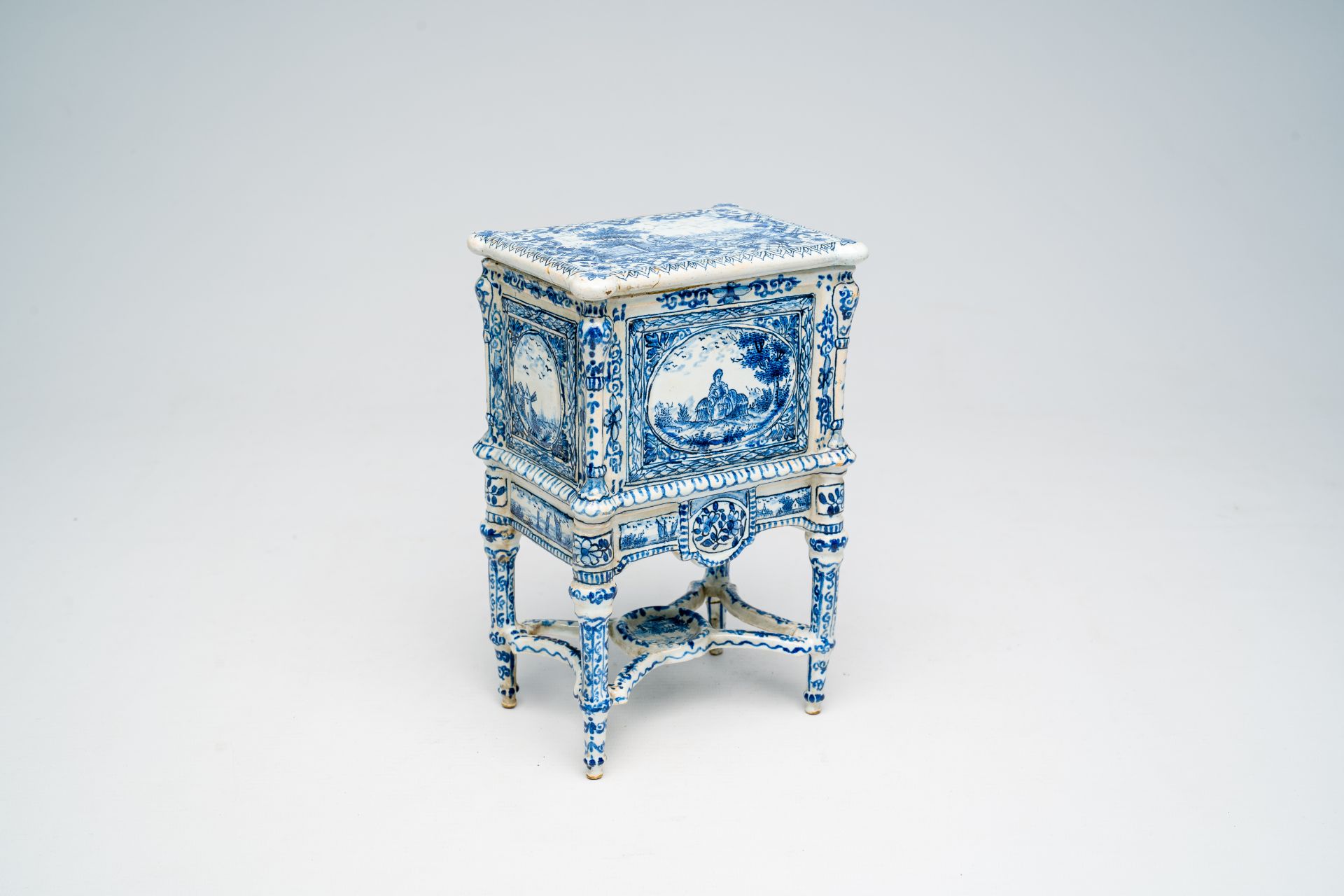 A French blue and white earthenware cabinet on stand with figures in a landscape and floral design,