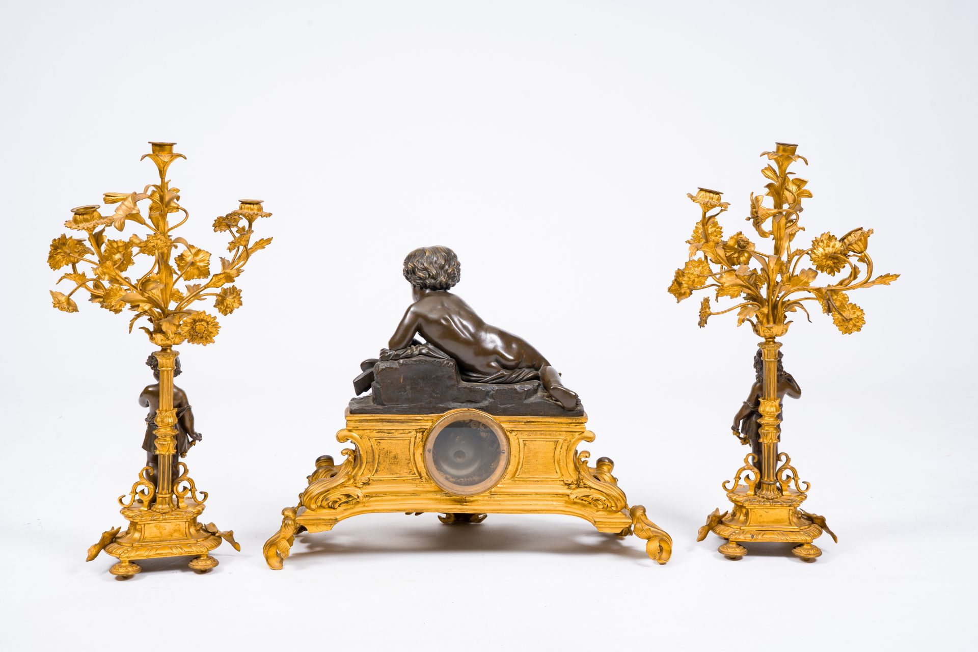 A French gilt and patinated bronze three-piece clock garniture crowned with a putto playing with a b