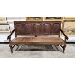 Late 18th/early 19th century oak settle with panelled seat and back, carved armrests and raised on