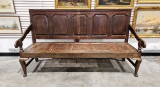 Late 18th/early 19th century oak settle with panelled seat and back, carved armrests and raised on