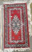Red ground rug with central geometric medallion 110cm x 58cm, single floral border and a Chinese