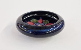 Moorcroft pottery small circular bowl with scroll over rim, decorated with a columbine on dark