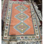 Persian style pink ground wool rug with three central stepped hooked lozenge medallions, multiple