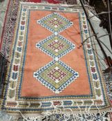 Persian style pink ground wool rug with three central stepped hooked lozenge medallions, multiple
