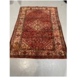 Eastern red ground rug with central hooked floral lozenge on herati field with floral spandrels,