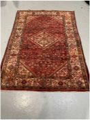 Eastern red ground rug with central hooked floral lozenge on herati field with floral spandrels,