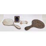 Two silver backed dressing mirrors, one repousse decorated, a miniature silver mounted picture frame