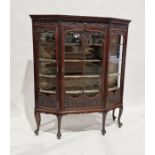 Edwardian mahogany display cabinet of canted form, the dentil cornice over a shell and acanthus