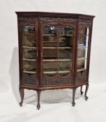 Edwardian mahogany display cabinet of canted form, the dentil cornice over a shell and acanthus