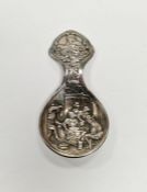 Continental white metal caddy spoon with embossed decoration depicting a traditional 19th century