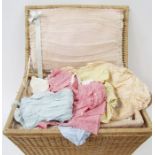 A vintage wicker nursery basket containing assorted mid and earlier 19th century baby clothes, to