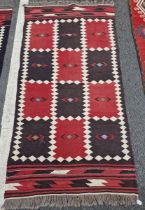 Two vintage Afghan rugs, each with chequerboard design in red and dark brown within cream lozenge-