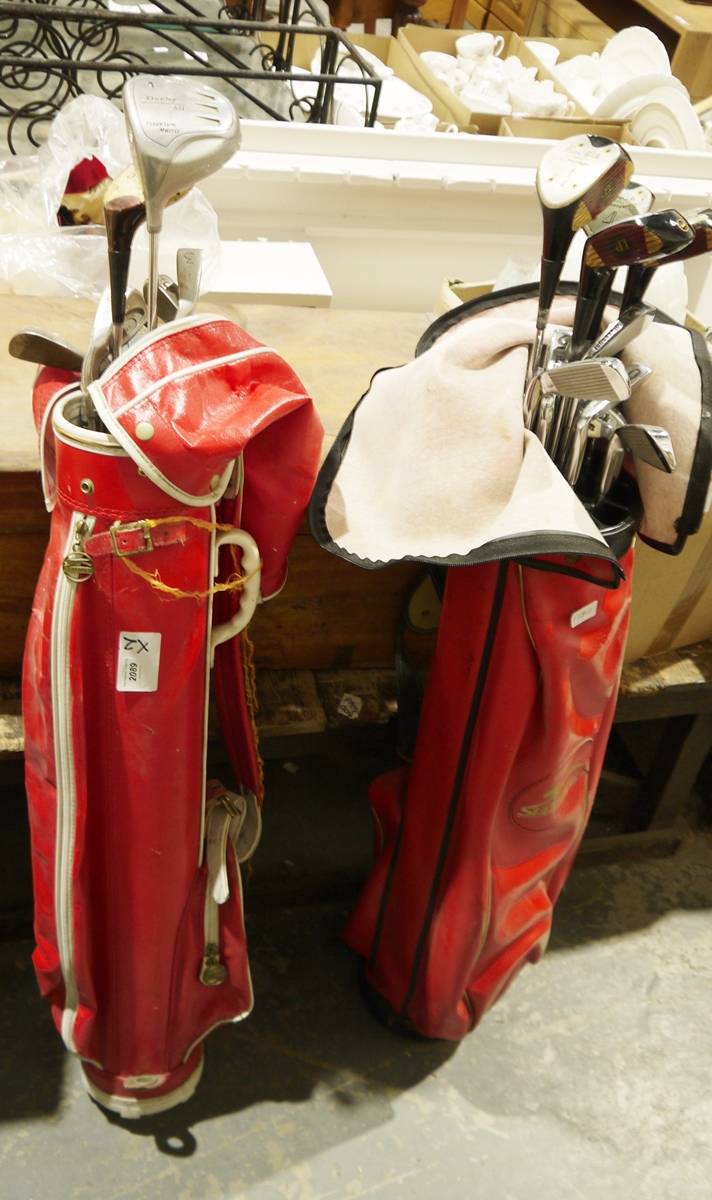 Two sets of golf clubs in red carry cases