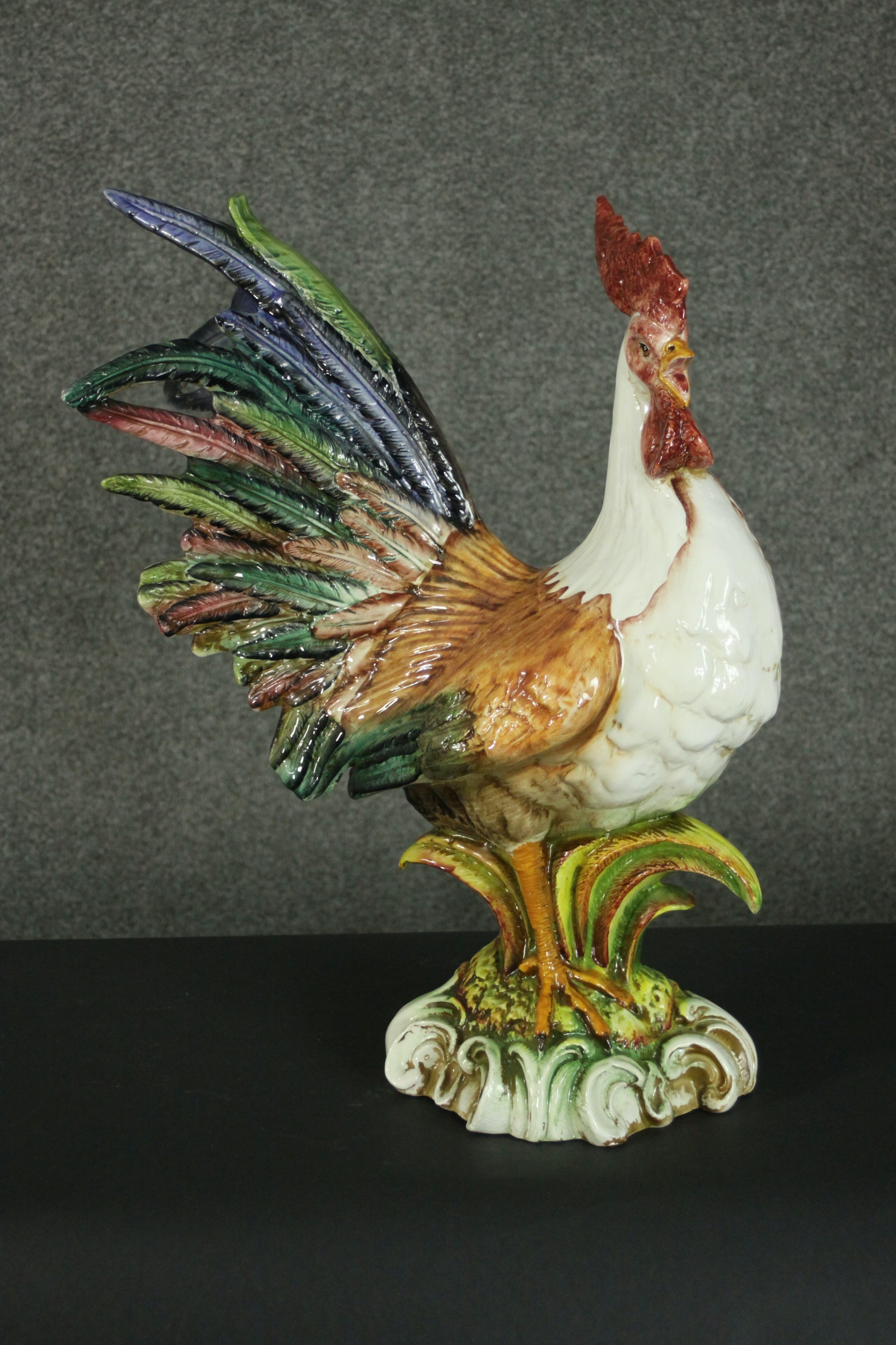 A large majolica pottery figure of a crowing cockerel, standing on a naturalistic base with a border