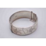 A silver wax filled engraved bangle with clip clasp and safety chain, decorated with a stylised