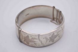 A silver wax filled engraved bangle with clip clasp and safety chain, decorated with a stylised