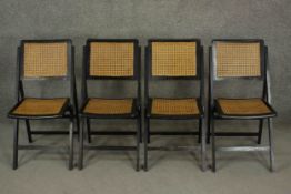 A set of four 20th century ebonised folding chairs, with caned backs and seats.