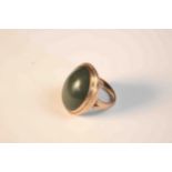 A pink metal (tests as 9ct gold) and green stone cabochon dress ring, set with an oval green