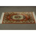 A Chinese woollen rug with central floral motif on terracotta ground. L.157 W.78cm.