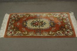 A Chinese woollen rug with central floral motif on terracotta ground. L.157 W.78cm.