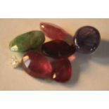 A collection of six mixed cut coloured gem stones, including rubies, emerald, sapphire and garnet.