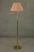 A contemporary brass reading lamp, with an adjustable arm and a pink shade, on a circular base. H.