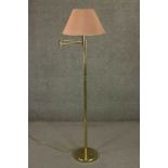 A contemporary brass reading lamp, with an adjustable arm and a pink shade, on a circular base. H.