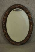 An early 20th century oval mirror, with a bevelled mirror plate, the frame carved and painted with