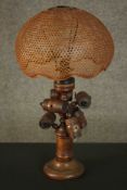 A treen turned pine table lamp, adorned with turned barrels, under a dome form caned shade. H.53 W.