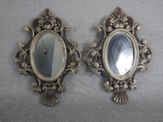A pair of Continental carved Baroque style mirrors, with an oval mirror plate in a silvered frame