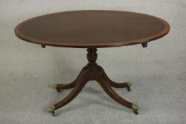 A George III style oval mahogany tilt top table, with a turned stem on a quatrefoil base with