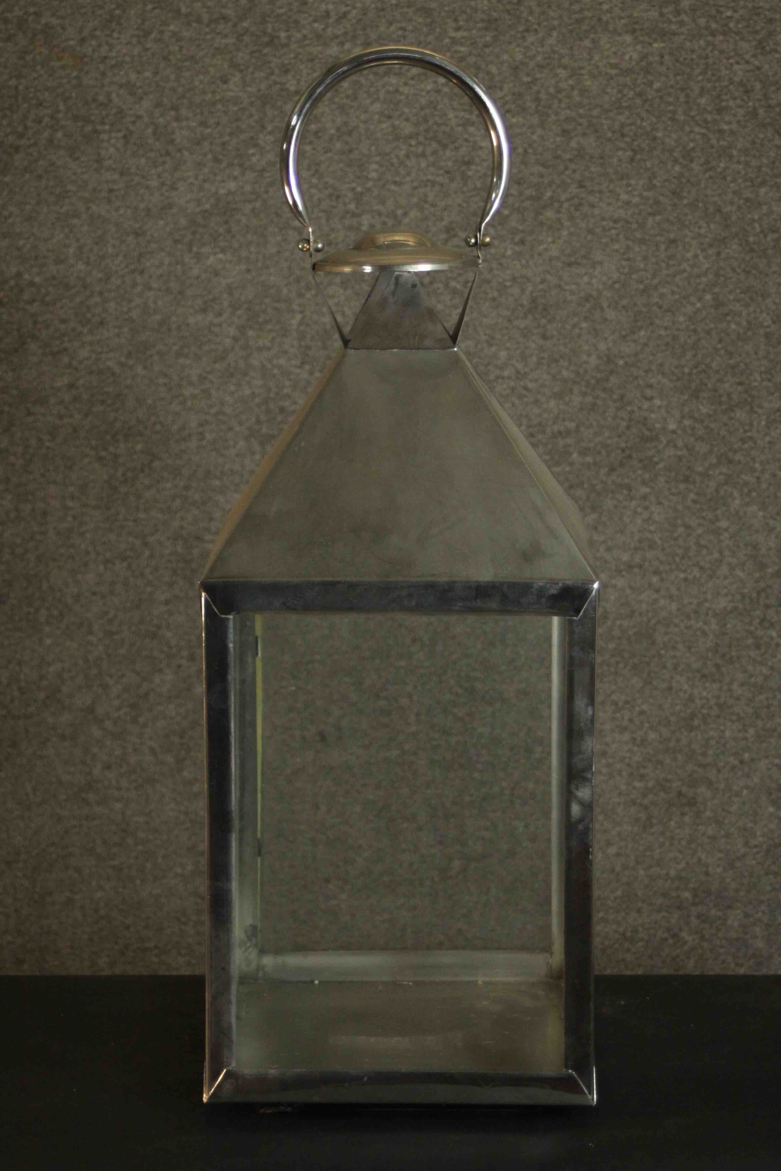 A contemporary nickel plated storm lantern, with a loop handle above a sloped top, with four