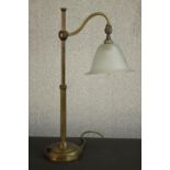 An early 20th century brass desk lamp, with an adjustable arm and a frosted glass shade, on a