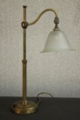 An early 20th century brass desk lamp, with an adjustable arm and a frosted glass shade, on a