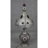 An Indian or Middle Eastern metalware lamp and shade, with embossed designs, glass panels and