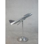 An Art Deco style polished metal model of a plane in flight on a stand with a circular base. H.79