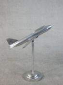 An Art Deco style polished metal model of a plane in flight on a stand with a circular base. H.79