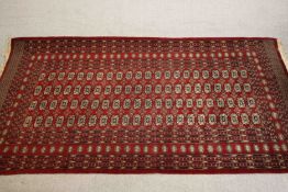 A Pakistan Bokhara carpet with repeating elephant's foot motif on a deep red ground within geometric