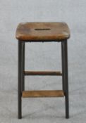 A 20th century industrial machinist's stool, with a tubular steel frame, wood seat and foot rests.