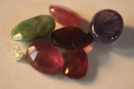 A collection of six mixed cut coloured gem stones, including rubies, emerald, sapphire and garnet.