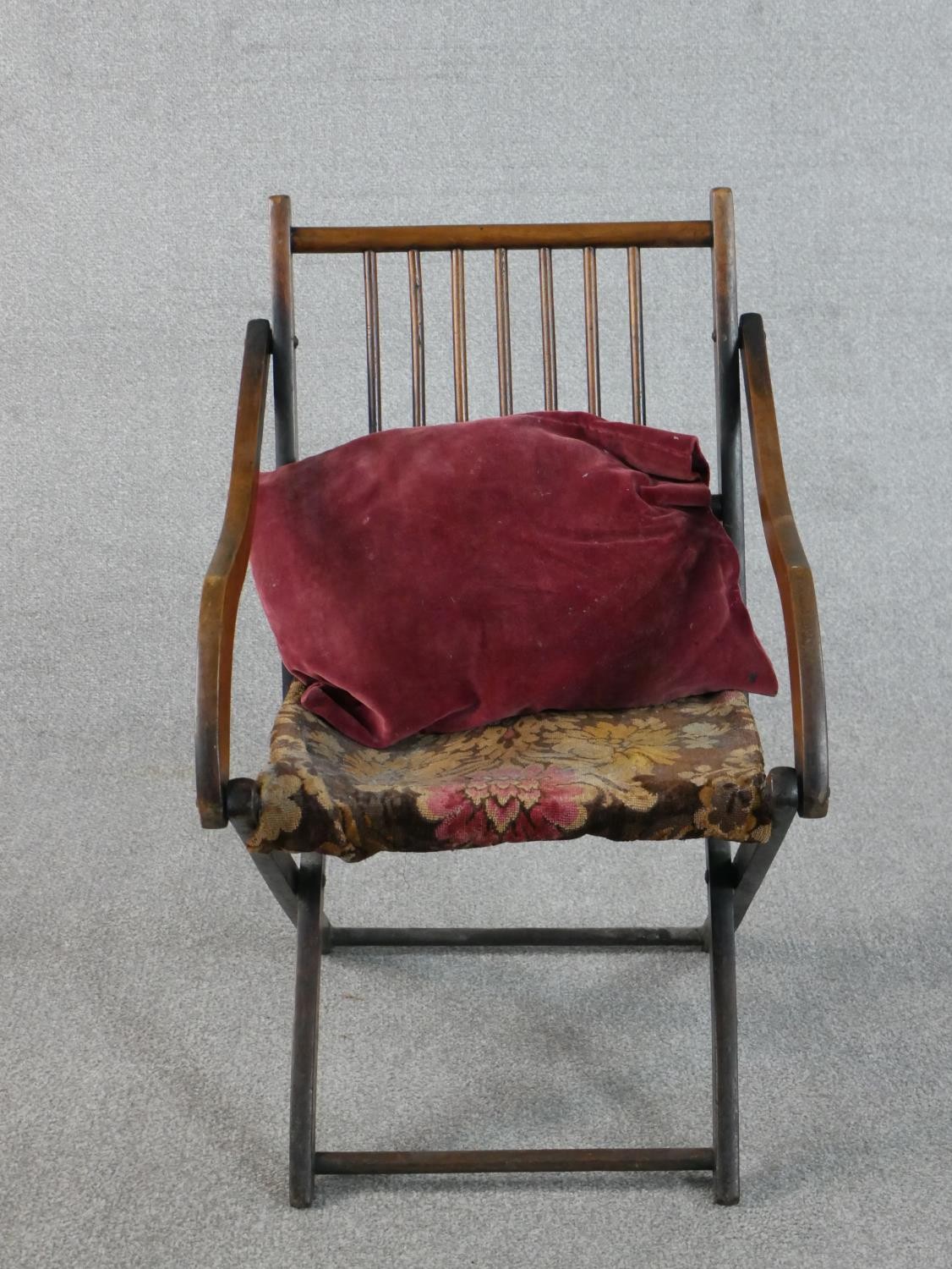 An early 20th century fruitwood folding armchair, with a spindle back, the seat upholstered in a