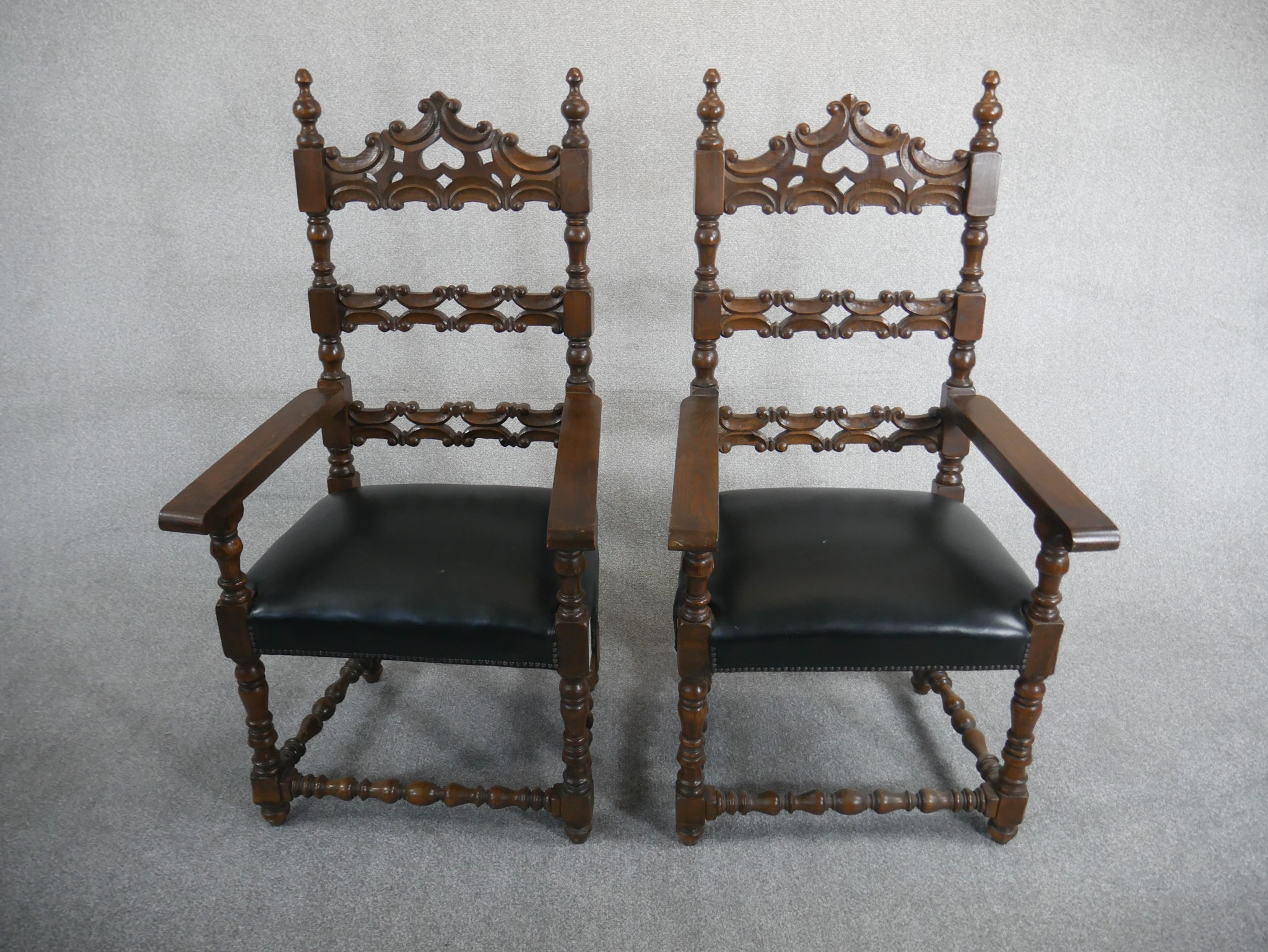 A pair of Spanish walnut ladder back carvers, the back carved with C scrolls over a black leather