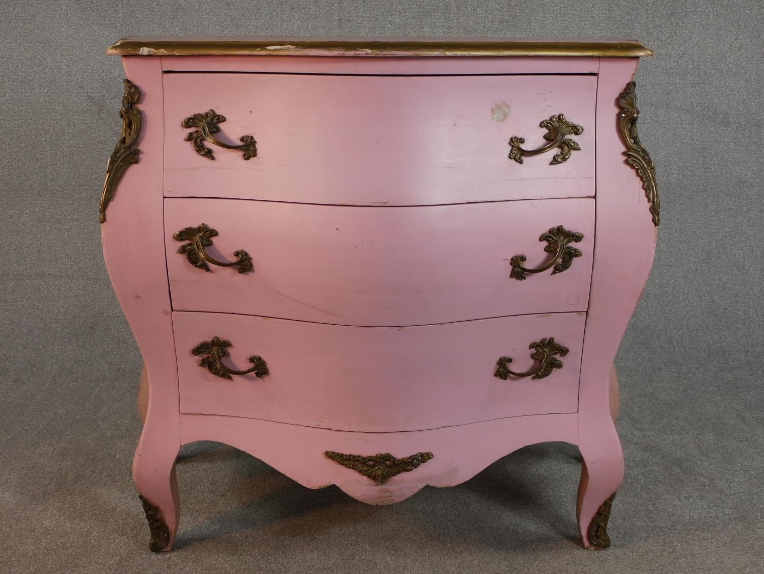A pink painted Louis XV style bombe chest of drawers, the top with a moulded parcel gilt edge over