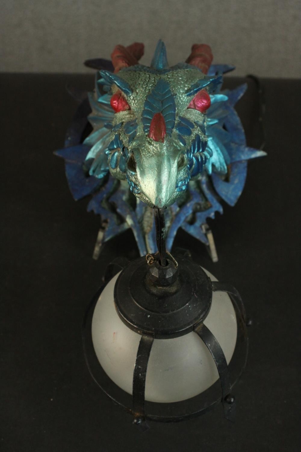 A moulded metallic painted dragon head wall lamp with caged frosted glass globe shade. H.33 W.23 D.