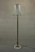 A 20th century brass standard lamp, with a cast tri-form base on a circular white marble plinth,