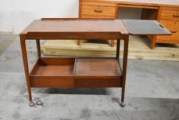 A vintage teak serving trolley with fold out top and fitted under tier. Two casters in need of