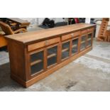 A large late 19th century oak shop display counter fitted with frieze drawers and glazed panel doors