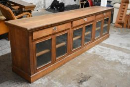 A large late 19th century oak shop display counter fitted with frieze drawers and glazed panel doors